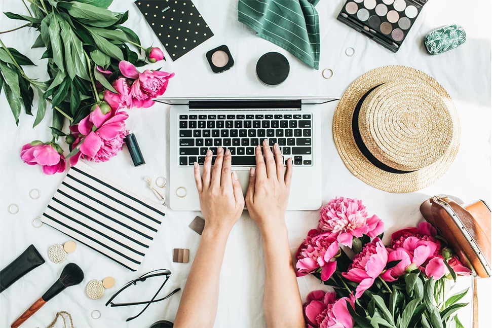 Computer surrounded by makeup and fashion items